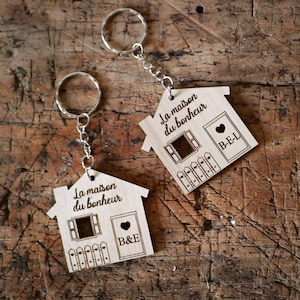 Peut inclure: Deux porte-clés en bois en forme de maison avec le texte "La maison du bonheur" et les initiales "B&E" et "B-E-L" gravées dessus.