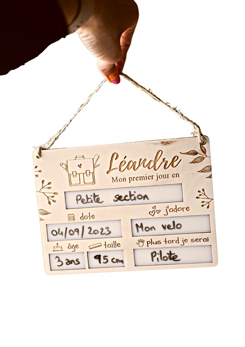 May include: A wooden sign with the name "L&eacute;andre" and the text "Mon premier jour en Petite section". The sign has spaces to fill in the date, age, and height. The date is filled in as "04/09/2023", the age is filled in as "3 ans", and the height is filled in as "95 cm". The sign also has a space to write what the child loves, which is filled in as "Mon velo", and a space to write what the child wants to be when they grow up, which is filled in as "Pilote".