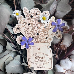 Les trous invitent à ajouter des fleurs, offrant ainsi une décoration à la fois pratique et émouvante. Offrez un cadeau unique et personnalisé à la maîtresse avec ce vase en bois gravé du message "Merci Maîtresse".