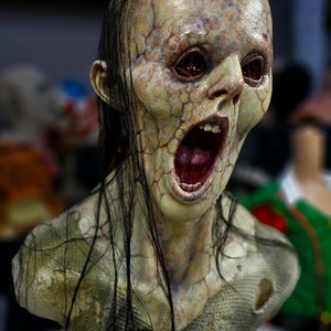 Könnte beinhalten: Eine detaillierte, realistische Büste eines Zombies mit langen schwarzen Haaren, blasser grüner Haut und einem weit geöffneten Mund, der rotes Zahnfleisch und Zähne zeigt. Die Augen des Zombies sind weit geöffnet und blutunterlaufen.