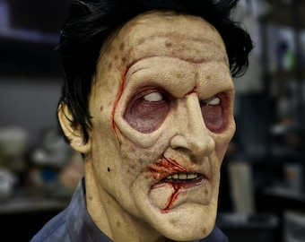 May include: A close-up of a realistic zombie mask with a detailed, gruesome appearance. The mask features a pale complexion, blood-red streaks, and a wide-open mouth with visible teeth. The mask is made of a high-quality material and is perfect for Halloween or cosplay.