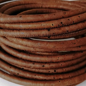 Può includere: Un rotolo di cordoncino in sughero marrone, un materiale naturale spesso utilizzato nell'artigianato e nella creazione di gioielli.