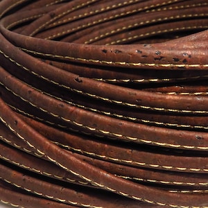 Puede incluir: Primer plano de un cordón de cuero de corcho marrón con costuras doradas. El cordón está enrollado en espiral.