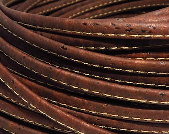 Può includere: Primo piano di un cordoncino in pelle di sughero marrone con cuciture dorate. Il cordoncino è arrotolato a spirale.