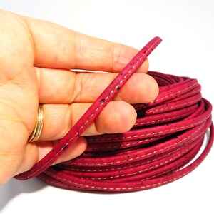 Puede incluir: Un rollo de cordón de corcho rojo con costuras doradas. El cordón tiene aproximadamente 5 mm de ancho y una textura moteada.