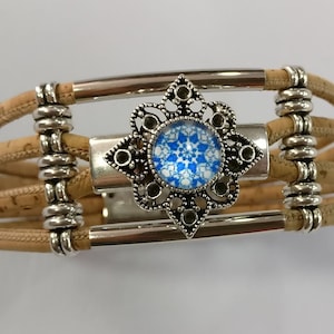 May include: A cork bracelet with a silver metal clasp and a decorative silver charm with a blue and white glass center.