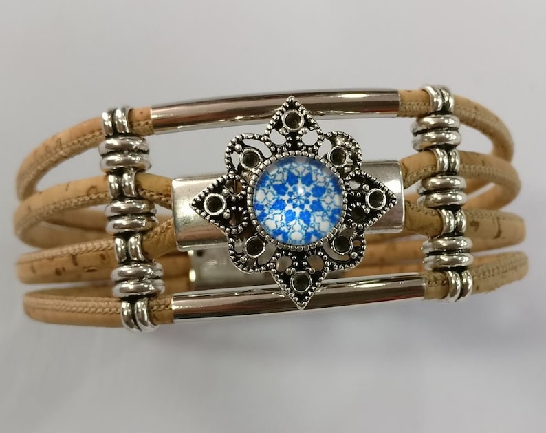 May include: A cork bracelet with a silver metal clasp and a decorative silver charm with a blue and white glass center.