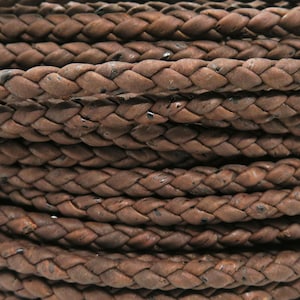 Puede incluir: Primer plano de una bobina de cordón de cuero trenzado marrón. El cordón está tejido apretadamente, con una superficie texturizada y variaciones de color visibles. El diseño trenzado es consistente, lo que sugiere un material duradero y decorativo.