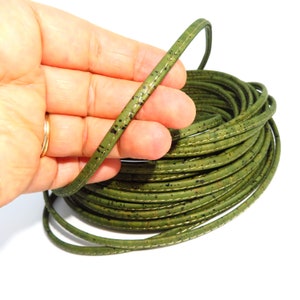 Puede incluir: Un rollo de ribete de corcho verde con un borde cosido. El ribete está hecho de corcho natural y tiene un aspecto moteado.