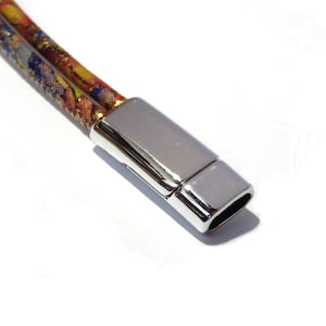 May include: Close-up of a silver magnetic clasp for a bracelet or necklace. The clasp is rectangular and has a smooth, shiny finish.