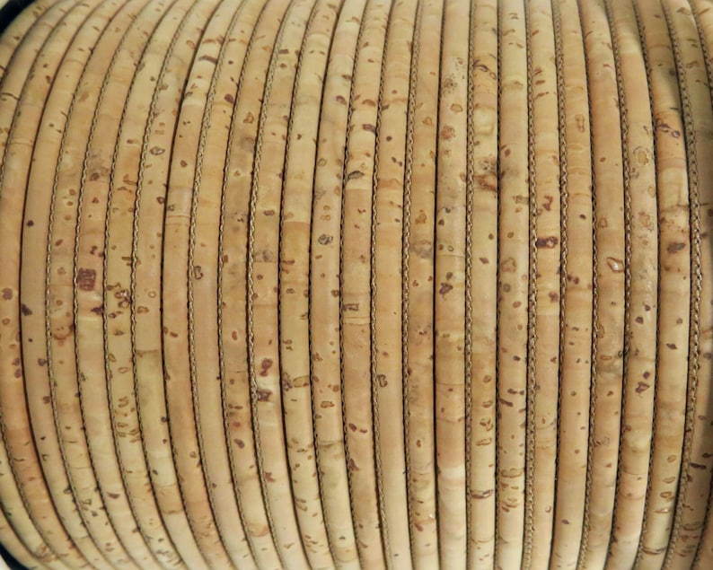 May include: Close-up of a roll of natural cork cord, a textured material with a light brown color. The cord is wound tightly in a spiral shape.