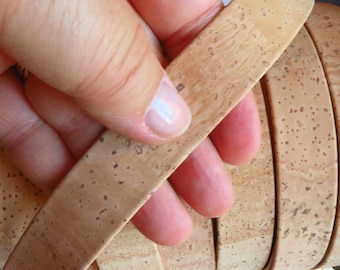 May include: A close-up of a stack of cork strips, each with a unique pattern of brown and beige flecks. The strips are held together by a hand, showcasing the natural texture of the cork.