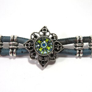 K&ouml;nnte beinhalten: Ein blaues und silbernes Armband mit einem dekorativen Metallanh&auml;nger mit einem bunten Blumenmuster.