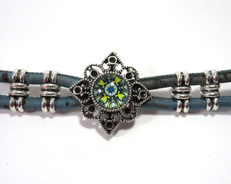 K&ouml;nnte beinhalten: Ein blaues und silbernes Armband mit einem dekorativen Metallanh&auml;nger mit einem bunten Blumenmuster.