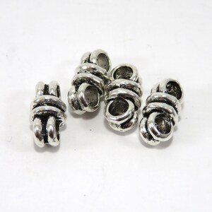 K&ouml;nnte beinhalten: Vier silberne Metallperlenkappen mit einem Knotendesign. Die Perlenkappen sind etwa 2,5 cm lang und haben ein Loch in der Mitte zum Einf&auml;deln.