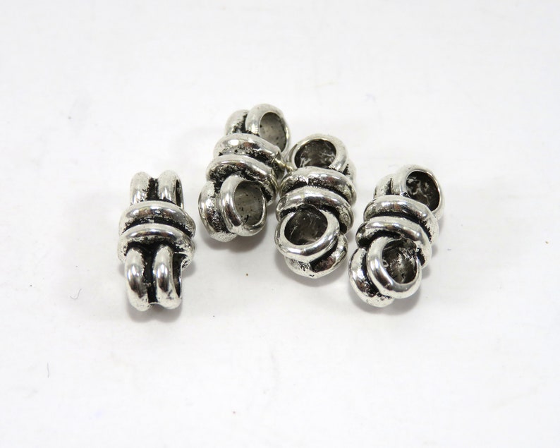 K&ouml;nnte beinhalten: Vier silberne Metallperlenkappen mit einem Knotendesign. Die Perlenkappen sind etwa 2,5 cm lang und haben ein Loch in der Mitte zum Einf&auml;deln.