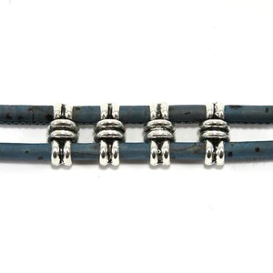K&ouml;nnte beinhalten: Ein doppelseitiges Armband aus Kork mit silberfarbenen Metallperlen. Die Perlen haben ein knotenartiges Design.