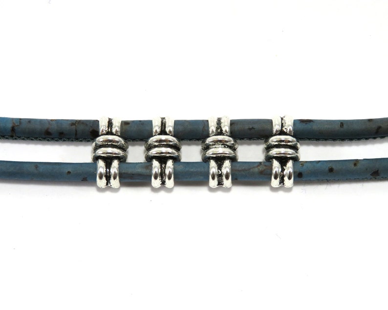 K&ouml;nnte beinhalten: Ein doppelseitiges Armband aus Kork mit silberfarbenen Metallperlen. Die Perlen haben ein knotenartiges Design.