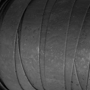 May include: A roll of dark charcoal grey cork material featuring a natural, porous texture with visible indentations and organic surface variations. The material is wound tightly in a continuous spiral, showcasing the layered edges of the strip.