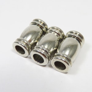 May include: Three silver metal barrel-shaped beads with a grooved design.