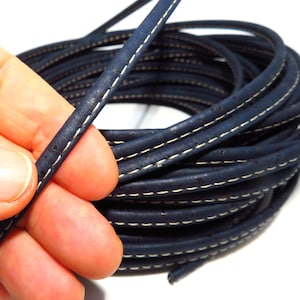 Puede incluir: Un rollo de cordón de cuero de corcho azul oscuro con costuras blancas. El cordón tiene aproximadamente 5 mm de ancho.
