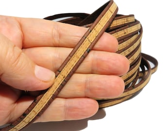Può includere: Cordoncino in pelle marrone con un'intarsio in sughero beige. Il cordoncino è arrotolato e tenuto in una mano.