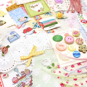 Op de afbeelding: Een verzameling knutselbenodigdheden waaronder een kaart met diverse kleurrijke knopen met het label Button it up, een klosje meerkleurig borduurgaren, kanten randen, stofresten met bloemen- en dessertpatronen, linten en kleine stoffen bloemen.