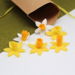 May include: Six felt flower embellishments, four yellow and two white, with orange centers. The flowers are arranged on a white surface.