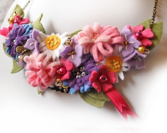 Puede incluir: Un collar de flores de fieltro de colores con flores rosas, moradas, blancas y amarillas. El collar está adornado con cuentas y un pequeño dije de mariposa.