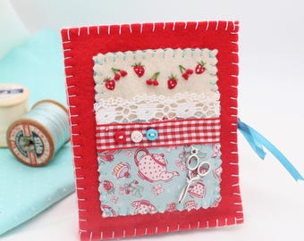 Puede incluir: Mantiene agujas de fieltro rojo con un tejido vintage de taza de té y estampado de fresa, encaje blanco, cinta de cuadros rojos y blancos y un par de tijeras plateadas.