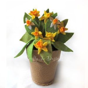 Peut inclure: Une composition florale en feutre dans un pot brun. Les fleurs sont jaunes et orange avec des centres blancs. Les feuilles sont vertes. Le pot est brun et a une texture en feutre. "Crafty Jo Designs" est écrit sur le pot.