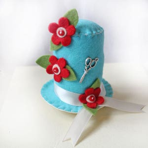 Alfiletero para sombrero de fieltro: artículo de costura turquesa con decoración floral.