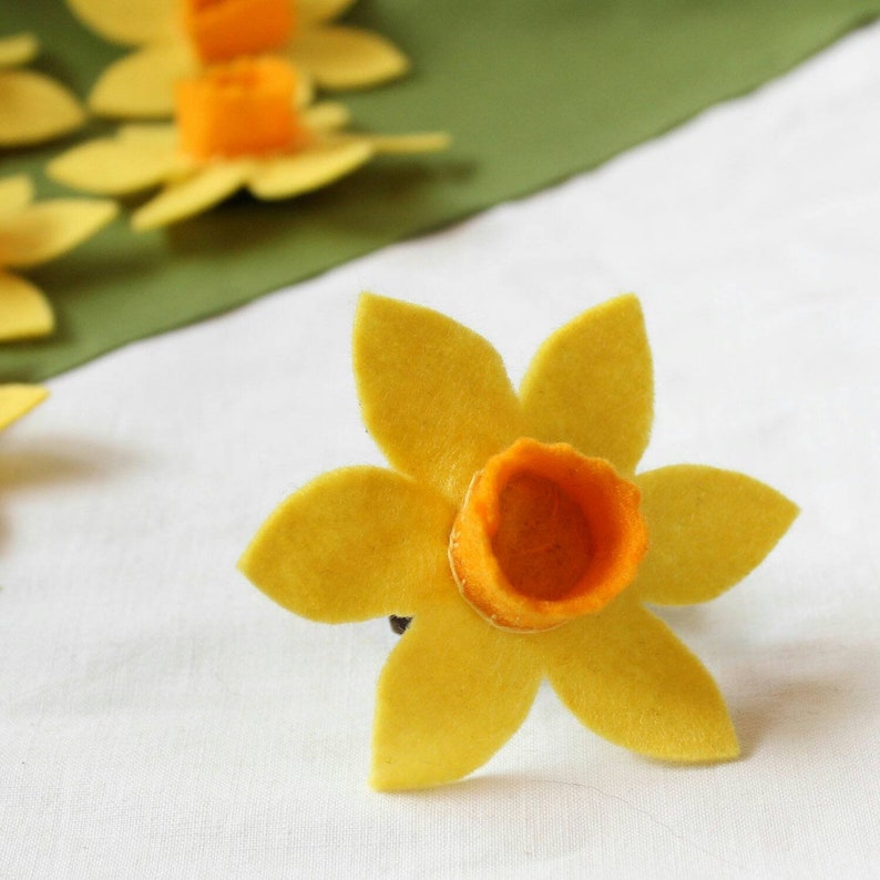 A felt daffodil flower with six yellow petals and an orange centre. The flower has an elastic back for attaching to a dog collar.