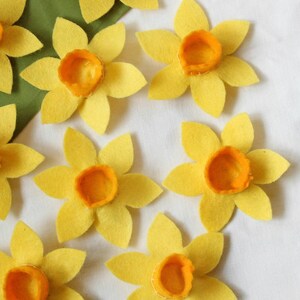 A close-up of eight felt daffodil dog collar decorations. The daffodils are yellow with orange middles.