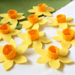 Nine yellow felt daffodils with orange centres. The daffodils are for attaching to a dog collar.