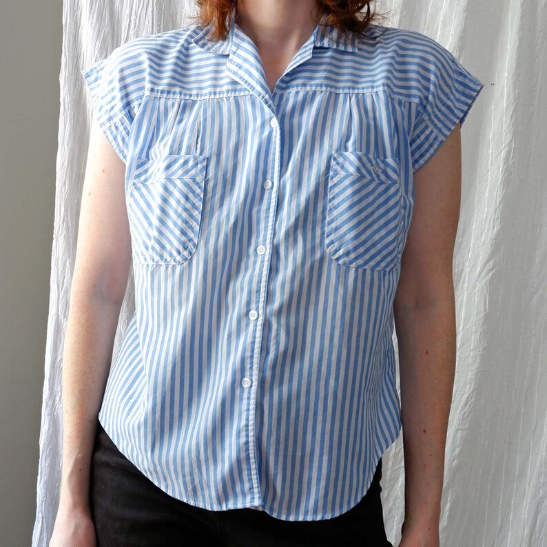 May include: A blue and white striped short-sleeved button-down shirt with two chest pockets.