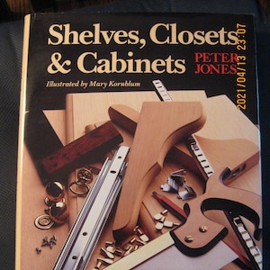 May include: A book titled "Shelves, Closets & Cabinets" by Peter Jones, illustrated by Mary Kornblum. The cover features a close-up of woodworking tools and materials, including a saw, a ruler, and wood pieces.
