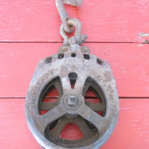 Könnte beinhalten: Eine antike, gusseiserne Rolle mit einem einzigen Rad und einem Haken. Die Rolle ist blau lackiert und trägt die Aufschrift "The Canton Pulley Co. Ohio".