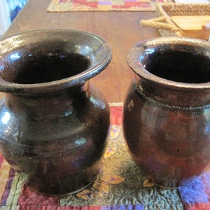 May include: Two brown ceramic vases with a glossy finish. The vases are sitting on a colourful patchwork quilt.