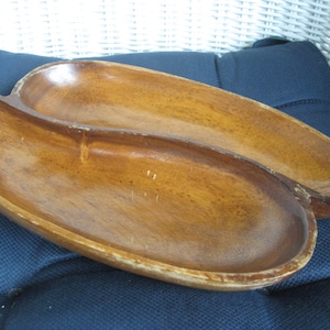 May include: A wooden serving dish with two separate sections, shaped like a teardrop. The dish is made of light brown wood and has a smooth, polished finish.