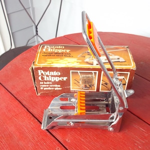 May include: Vintage potato chipper with chrome-plated metal and orange accents. The box reads "Potato Chipper" with "40 holes cutter-section & pusher-plate". The chipper is designed to cut potatoes into uniform strips. The chipper is on a red wooden table.