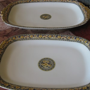 May include: Two white oval serving platters with gold trim and floral designs. The platters have a raised rim and a center floral design.