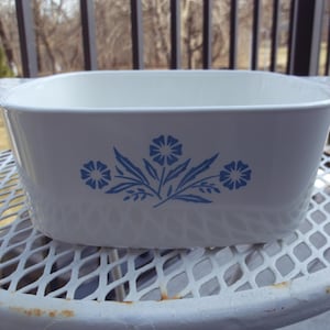 May include: A white ceramic mug with a black handle and the text "But First, Coffee" in a bold, black font. The mug is set against a blurred background, suggesting a cozy setting.