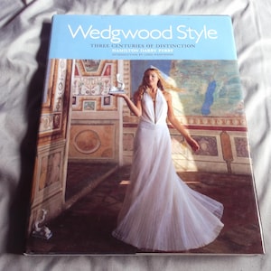 May include: A book titled "Wedgwood Style: Three Centuries of Distinction" with a light blue cover. The cover features a woman in a white dress holding a small sculpture. The background shows a mural.