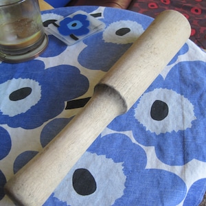 May include: A wooden rolling pin on a blue and white floral tablecloth. The rolling pin is made of light-colored wood and has a smooth surface.