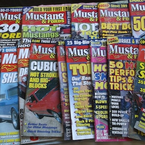 以下が含まれることがあります： ヴィンテージの「Mustang & Fords」雑誌のコレクション。表紙には大胆なテキスト、車のイラスト、そして「Hot Mustangs」や「50 Fastest」などのタイトルが掲載されています。雑誌は赤、黄色、青など様々な色があります。