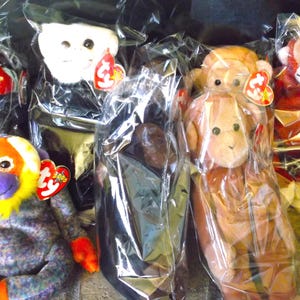 May include: A collection of six plush toys in various colors and designs, including a black and white monkey, a brown monkey, a yellow and purple monkey, a white monkey, a brown monkey, and a red monkey. The toys are all wrapped in clear plastic bags and have Ty tags attached.