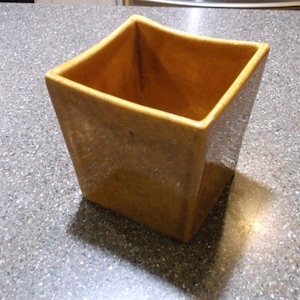 May include: A square, light brown ceramic planter with a slightly flared top. The planter has a textured surface and is designed with a modern aesthetic. Ideal for indoor or outdoor use, it adds a touch of elegance to any space.