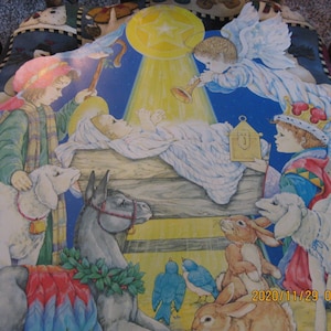 May include: A vintage Christmas nativity scene with a baby Jesus in a manger, a donkey, a sheep, and three wise men. The scene is painted on a fabric backdrop with a star and a bright light shining down.