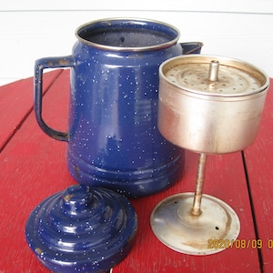 Può includere: Caffettiera in smalto blu con coperchio e filtro in metallo. La caffettiera ha una finitura in smalto blu macchiettato. Il filtro ha una base in metallo e una parte superiore in metallo con fori.